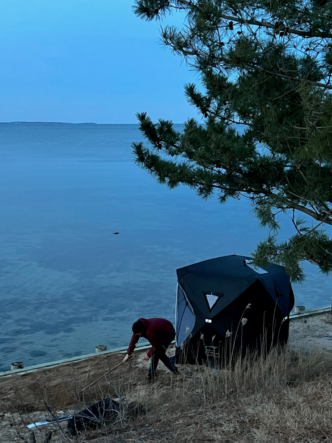 Image of a person gathering wood to feed a wood-fired sauna stove with Ox Sweat portable tent sauna burning hot and on a beach. 