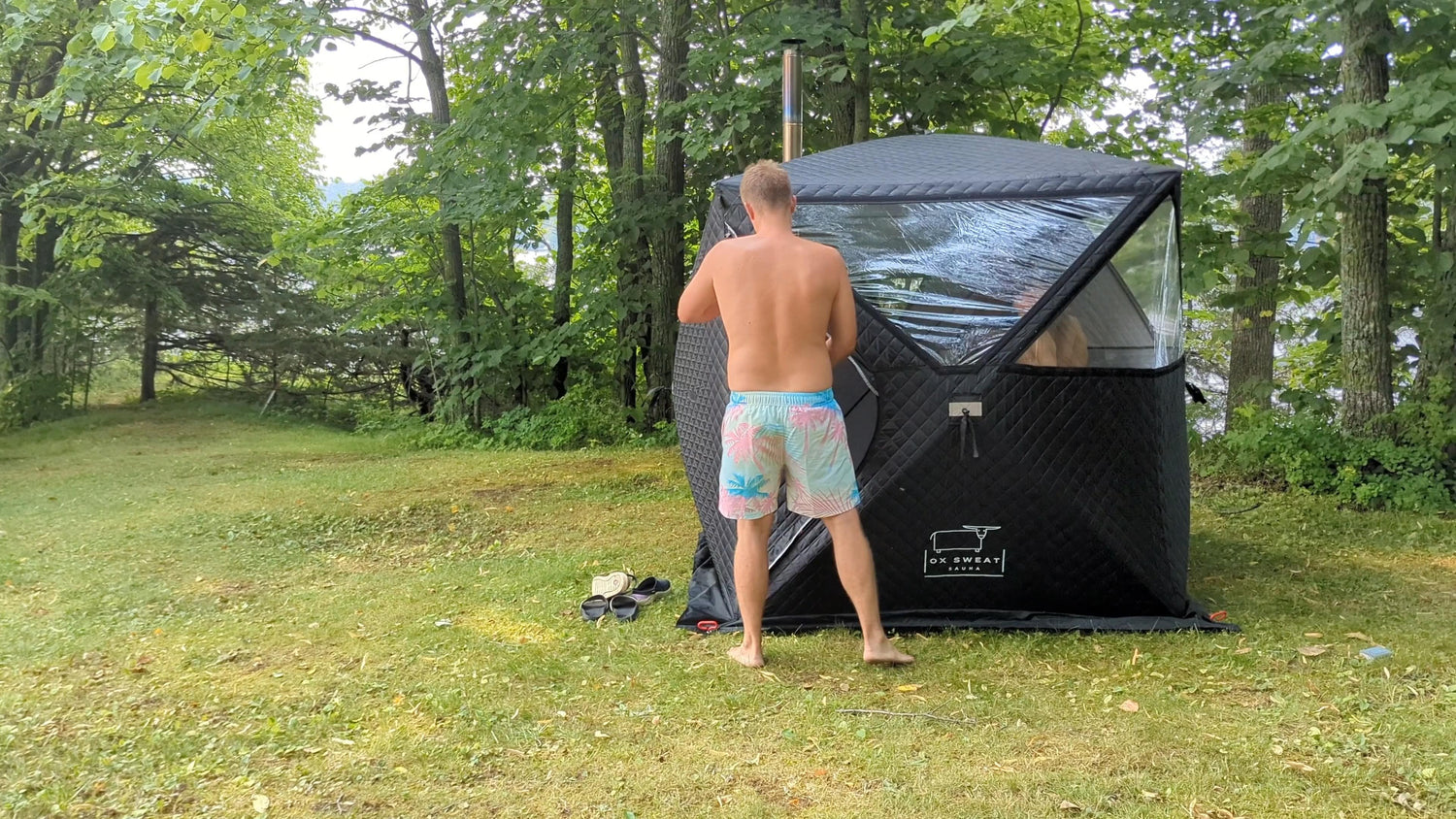 A stunning image of a portable sauna set amidst a breathtaking outdoor backdrop. A happy camper is seen relaxing inside the sauna, surrounded by nature's beauty.